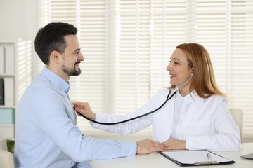 Cardiologist with stethoscope listening patient's heartbeat at desk in hospital