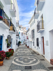 Fototapeta premium Charming cobblestone street with white houses and colorful flowers in the picturesque village of Frigiliana, Andalusia, Spain on a sunny day with blue sky