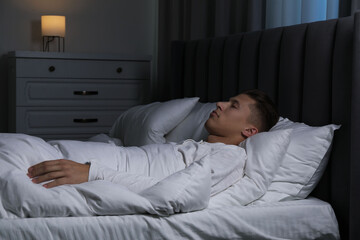 Fototapeta premium Young man sleeping in soft bed at night