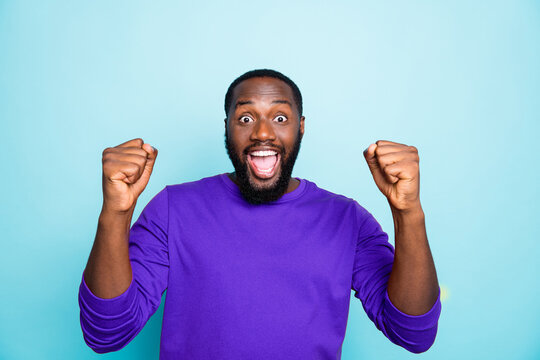 Photo of amazing dark skin guy celebrating lottery winning raising fists yelling triumphing wear casual orange pullover isolated blue color background