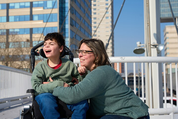 Happy boy with disability smiling with his mother on a bridge in the city
