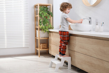 Little boy standing on step stool near bathroom vanity indoors