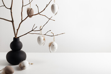 Easter composition with modern vase and decorative eggs hanging on the twigs. Easter natural background, copy space for your text.
