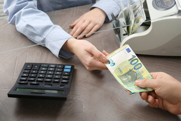 Client giving euro banknotes to cashier at table in money exchange, closeup