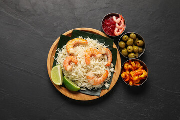 Pieces of banana leaf with rice, shrimps and lime among other food and sauce on grey textured table, flat lay