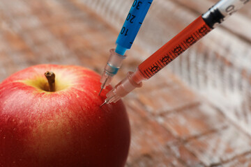 GMO concept. Red apple with syringes on blurred background, closeup