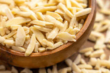 Chopped almonds in rustic wooden bowl with scattered nut pieces
