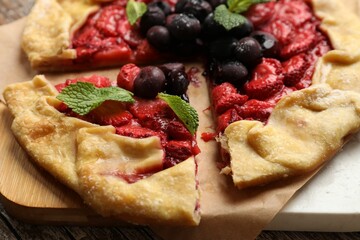 Tasty galette with strawberries, blueberries and mint on table, closeup