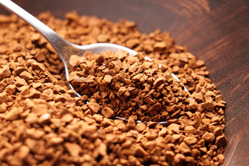 Particles of granulated instant coffee in rustic wood bowl with metal spoon