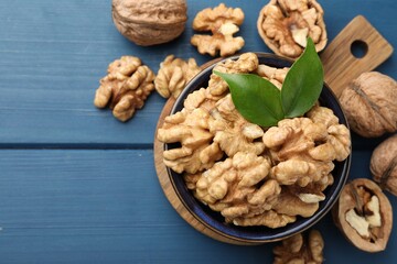 Fresh walnuts and green leaves in bowl on blue wooden table, flat lay. Space for text