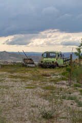 Abandoned Vintage Truck and Wooden Cart in a Rural Landscape under a Stormy Sky. A nostalgic scene featuring an old, rusted green truck and a weathered wooden cart in a remote countryside setting.