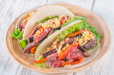 Three carne asada tacos filled with steak, grilled peppers, lettuce, and cheese