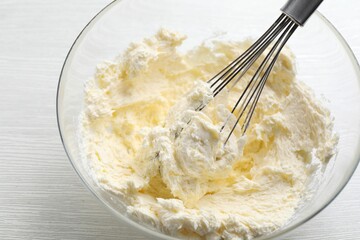 Bowl with whisk and whipped cream on white wooden table, closeup