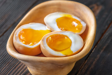 Halved ajitsuke tamago ramen eggs with golden yolks in wooden bowl