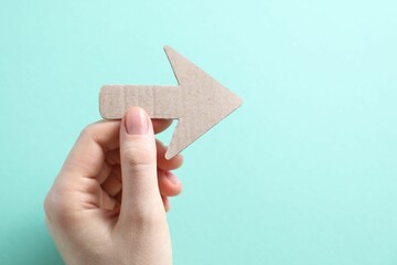 Woman with paper arrow on turquoise background, top view. Space for text