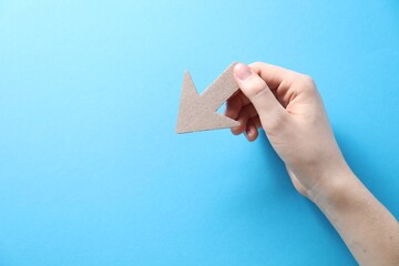Woman with paper arrow on light blue background, top view. Space for text