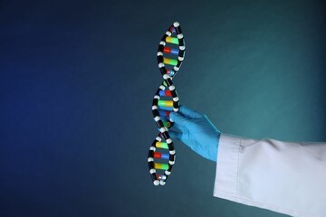 Scientist with DNA structure model on dark blue background, closeup
