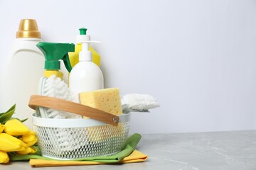 Spring cleaning. Detergents, supplies and tulips on light grey table against white background, space for text