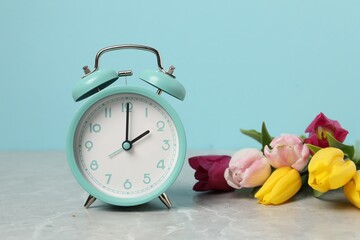 Spring time. Alarm clock and beautiful tulips on grey marble table against light blue background