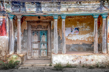 Weathered old building facade with intricate blue and white wooden door and worn columns showcasing historical decay and urban charm
