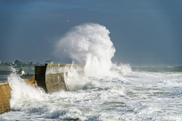  À Lesconil, les vagues furieuses s'écrasent sur la jetée sous un ciel bleu éclatant. L'écume blanche se dresse en volutes spectaculaires, capturant la puissance brute de l'océan.
