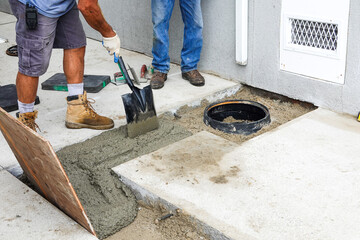 Men repairing a trench cut in a concrete driveway with wet cement and using a shovel