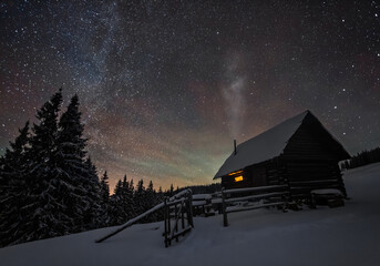 Winter landscape. Sky with stars. Mystical night. Old wooden hut on the lawn covered with snow. Forests. New Year's  house in the evening.  Wallpaper background. Location place Carpathian, Ukraine