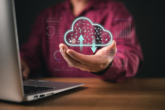 A man uses a laptop while holding a futuristic holographic cloud icon with upload and download symbols. The digital interface represents cloud computing, data storage, and tech innovation. - Powered by Adobe