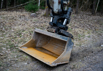 Heavy-duty excavator bucket with hydraulic mechanism resting on muddy forest ground