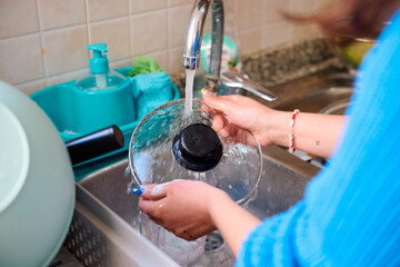 Washing glass cookware in a modern kitchen sink while water flows steadily
