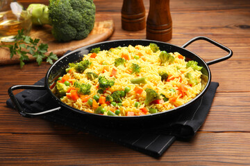 Tasty rice with vegetables in baking dish on wooden table, closeup