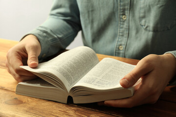 Naklejka premium Man reading Holy Bible in English language at wooden table, closeup