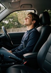 A young man relaxes in a parked car, smiling and enjoying the calm outdoors on a sunny day