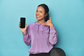 Filipina ready for gym with phone on blue showing a mobile phone call gesture with fingers.