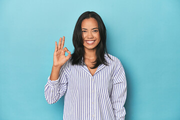 Filipina young woman on blue studio cheerful and confident showing ok gesture.