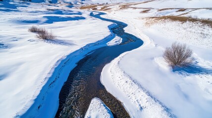 Fototapeta premium Aerial view of winding river flowing through snow-covered landscape in winter