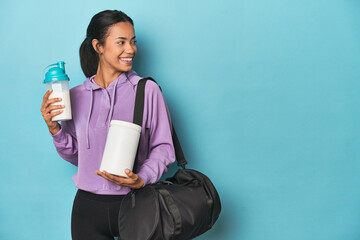 Filipina athlete with protein shake and powder on blue studio