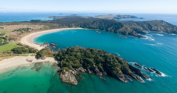 Stunning aerial view of a secluded Matai Bay. Tranquil turquoise water laps a pristine sandy beach, framed by lush green hills. Coastal beauty. Karikari Peninsula, Northland, NZ