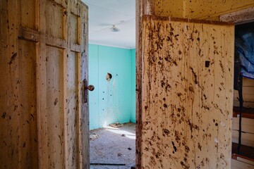 Abandoned room, teal walls, and dirty, stained beige walls. Sunlight streams in, highlighting the...