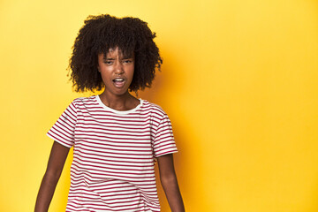 Teen girl in red striped T-shirt, yellow studio backdrop shouting very angry, rage concept,...