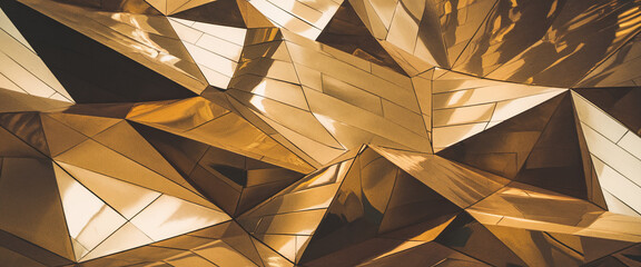 Close-up of a reflective geometric golden surface with sharp triangular facets and smooth polished textures, representing modern luxury and contemporary design. 3D wallpaper