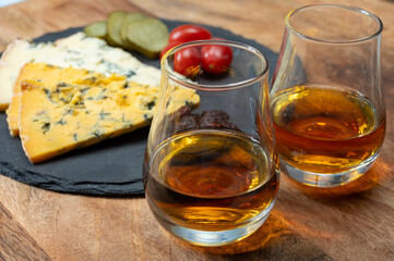 Whiskey and cheese pairing, tasting whisky glasses and plate with sliced crumbly old blue stilton and blue shropshire cheeses, Great Britain food and drink