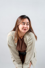 Obraz premium A young woman in a cozy sweater leans forward with a curious and playful expression, looking to the side against a neutral background