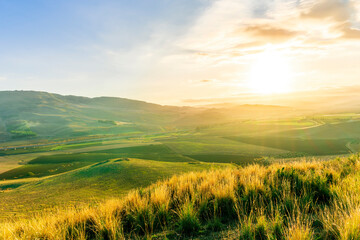 Fototapeta premium spring season green landscape of green field and meadow in a hill countryside with mountains and beautiful sunset sky on background