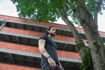 Young tattooed man portrait outdoors with nature and parking lot in the background