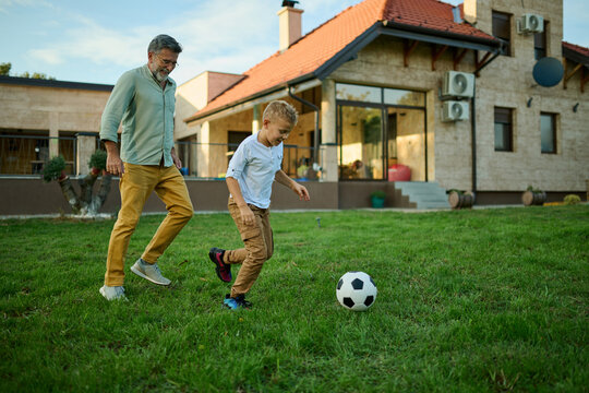 Grandfather and grandson playing soccer in backyard of house
