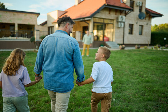 Father walking away holding hands with two kids in backyard