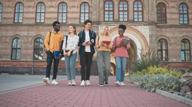 Group of students walking together towards camera. Everyone talking. Telling jokes or discussing past lectures. Building plans for weekend. Friendly community. Looking at each other.
