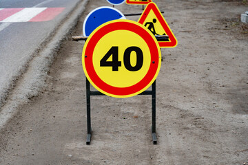 A bright yellow speed limit sign indicates a 40 km/h restriction near a construction area, surrounded by warning signs