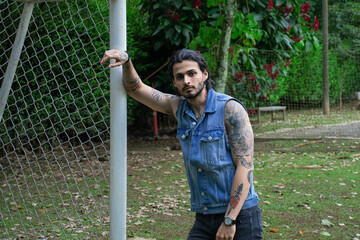 Young tattooed man standing next to a soccer goal in a park surrounded by nature